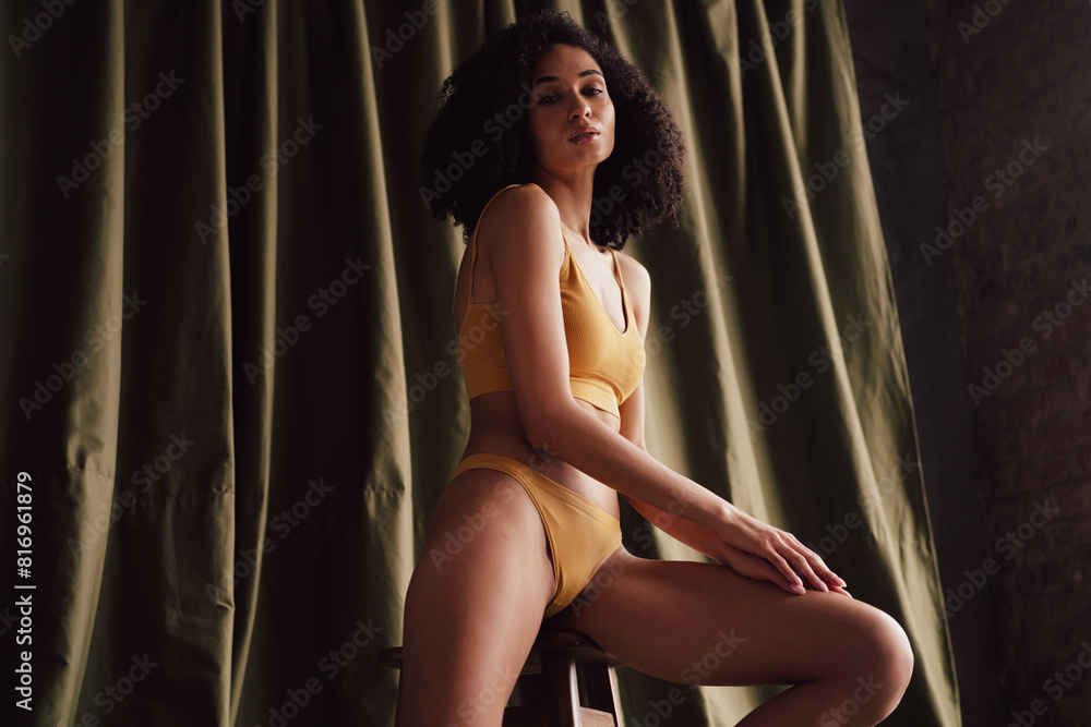 Unretouched portrait of gorgeous model girl sit chair touch leg khaki curtain background