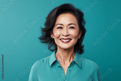 Portrait of a tender asian woman in her 50s smiling at the camera on soft teal background