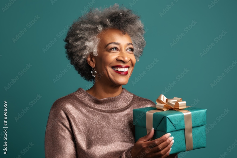 Portrait of a glad afro-american woman in her 50s holding a gift over soft teal background Portrait of a glad afro-american woman in her 50s holding a gift over soft teal background