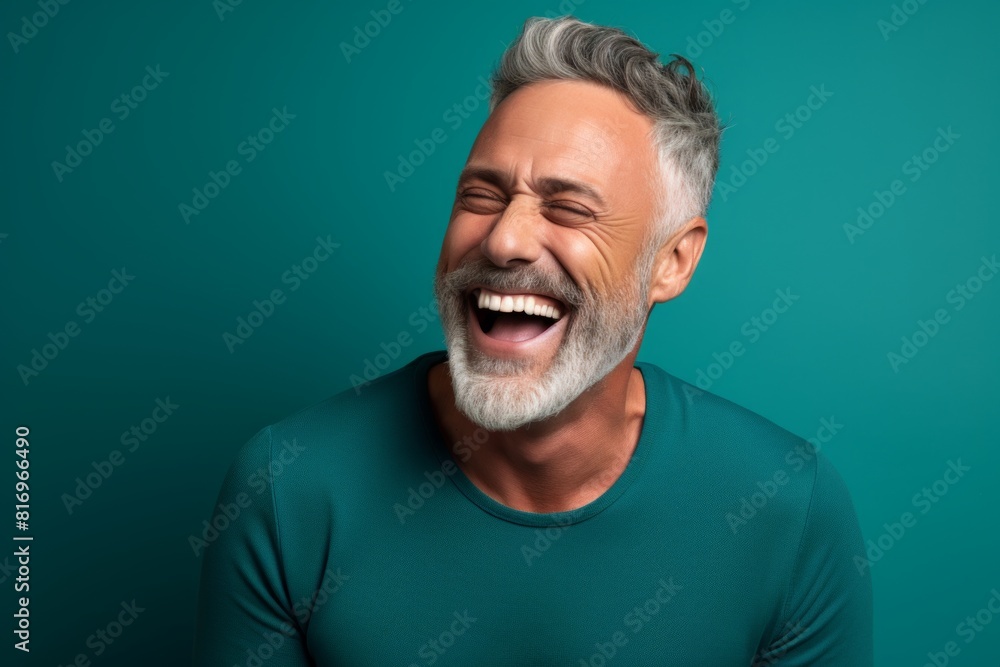 Obraz premium Portrait of a happy man in his 50s laughing over soft teal background