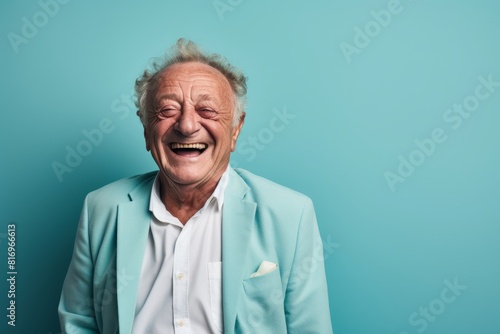 Portrait of a satisfied man in his 80s laughing in soft teal background