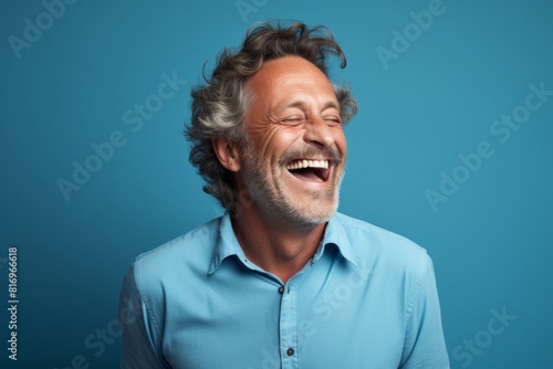 Portrait of a happy man in his 50s laughing in front of soft teal background