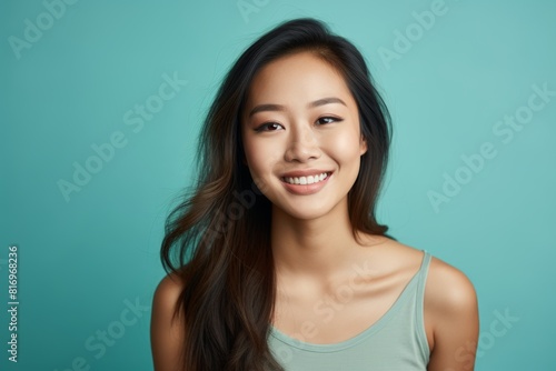 Portrait of a smiling asian woman in her 20s smiling at the camera on soft teal background