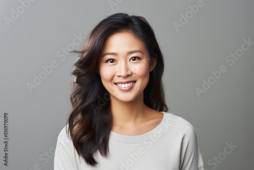Portrait of a smiling asian woman in her 30s smiling at the camera isolated in soft gray background
