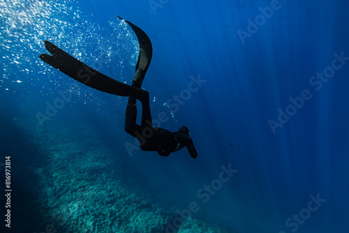 Freediver Swimming in Deep Sea With Sunrays. Young Man Diver Eploring Sea Life.