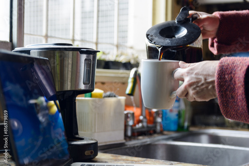 close up of an Unrecognizable Person is pouring coffee into a mug from a coffee maker in the kitchen
