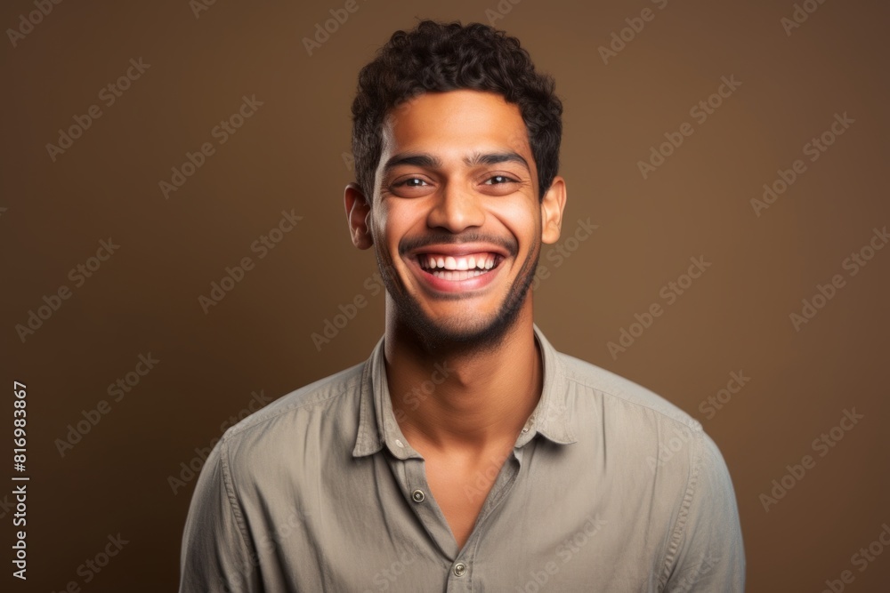 Obraz premium Portrait of a grinning indian man in his 20s smiling at the camera on soft brown background