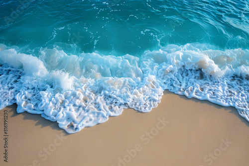 A top view of the crystal-clear azure sea  white wave foam  and beautiful sandy beach on a sunny day