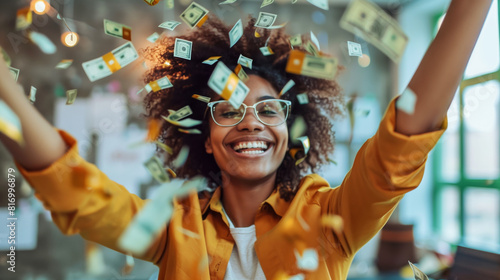 A joyful person wearing glasses and a yellow shirt is smiling broadly while surrounded by flying money in a bright, cheerful environment. photo
