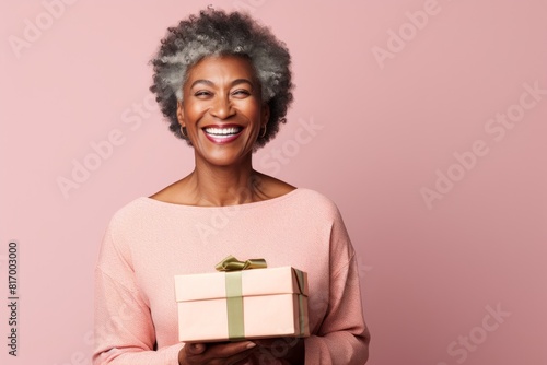 Portrait of a grinning afro-american woman in her 70s holding a gift in front of pastel or soft colors background © Markus Schröder