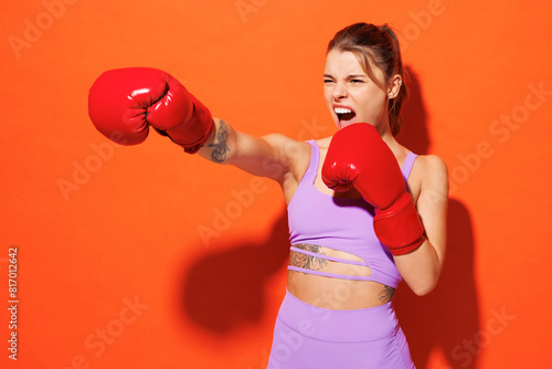 Side view young fitness trainer instructor sporty woman sportsman wear purple top clothes red gloves spend time in home gym boxing isolated on plain orange background. Workout sport fit abs concept. photo