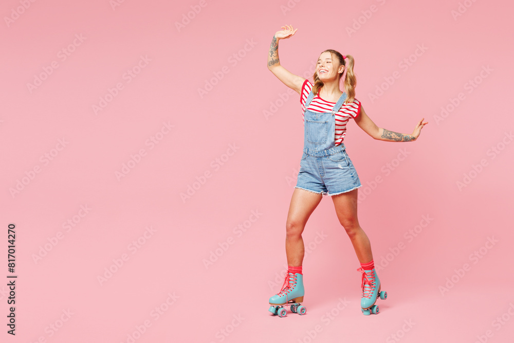 Full body side view young happy woman wear red t-shirt denim overalls casual clothes blue rollers rollerblading waving hand isolated on plain pink background. Summer sport lifestyle leisure concept. Full body side view young happy woman wear red t-shirt denim overalls casual clothes blue rollers rollerblading waving hand isolated on plain pink background. Summer sport lifestyle leisure concept.