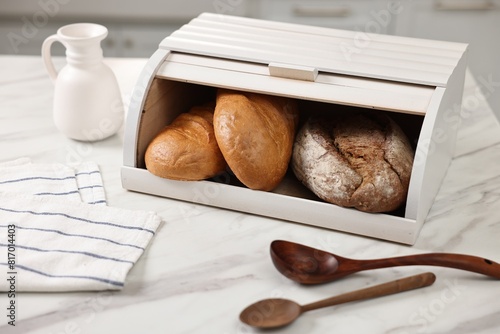 Wooden bread basket with freshly baked loaves and spoons on white marble table in kitchen photo