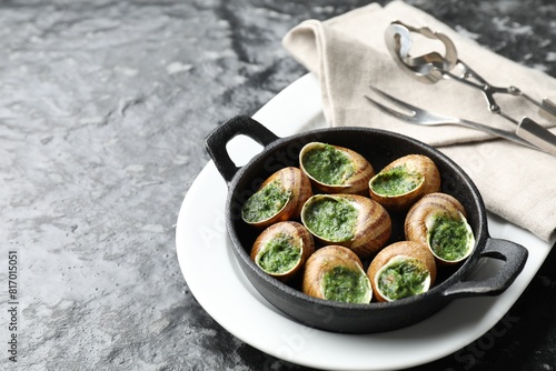 Delicious cooked snails in baking dish served on grey textured table. Space for text