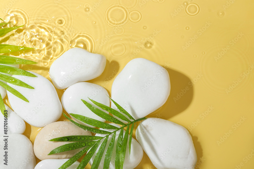 Spa stones and palm leaves in water on yellow background, flat lay