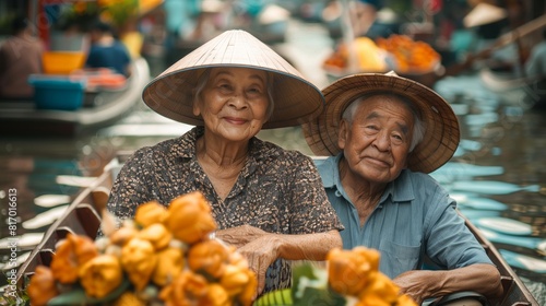 Elderly couple wearing conical hats, sitting in a boat filled with oranges Surrounded by boats and various stalls, the boat market