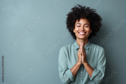 Portrait of a blissful afro-american woman in her 40s joining palms in a gesture of gratitude isolated in minimalist or empty room background