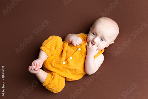 small child sucking fingers on a brown background. portrait of a newborn boy. baby's first photo shoot
