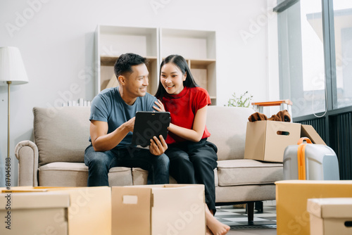 Asian young attractive couple man and woman use tablet and smartphone online shopping furniture decorate house with carton package move in new house. married asian moving home. . © Nuttapong punna