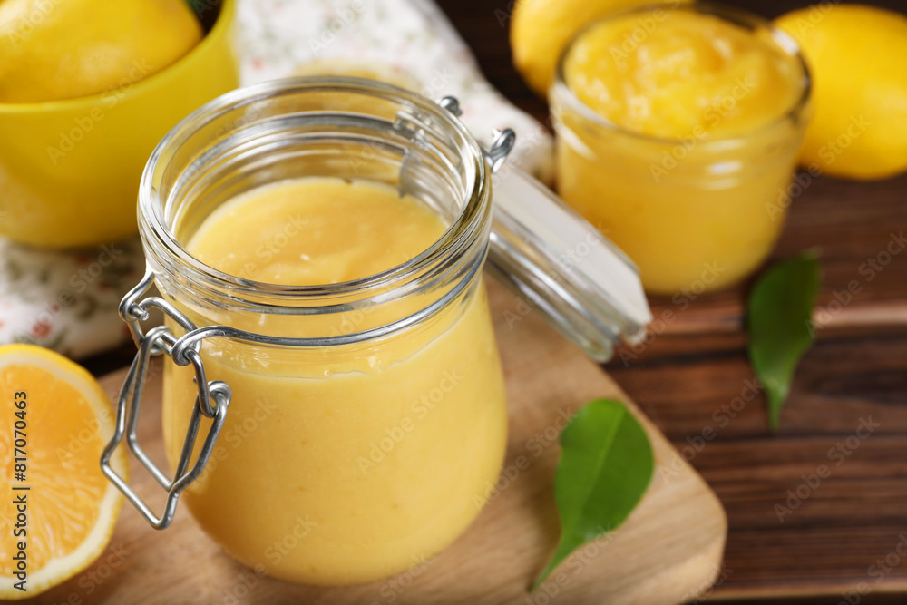 Delicious lemon curd in glass jars, fresh citrus fruits and green leaves on wooden table, closeup Delicious lemon curd in glass jars, fresh citrus fruits and green leaves on wooden table, closeup