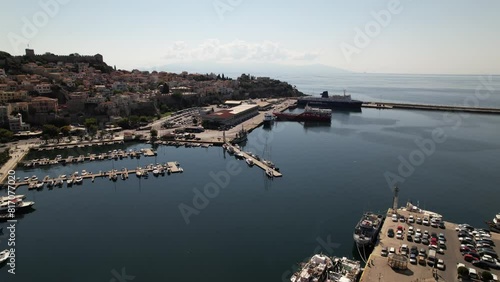 Witness a bustling harbor from above, as boats of all sizes peacefully dock in Kavala, Greece. The shimmering water, colorful vessels, and lively atmosphere combine to create a captivating scene