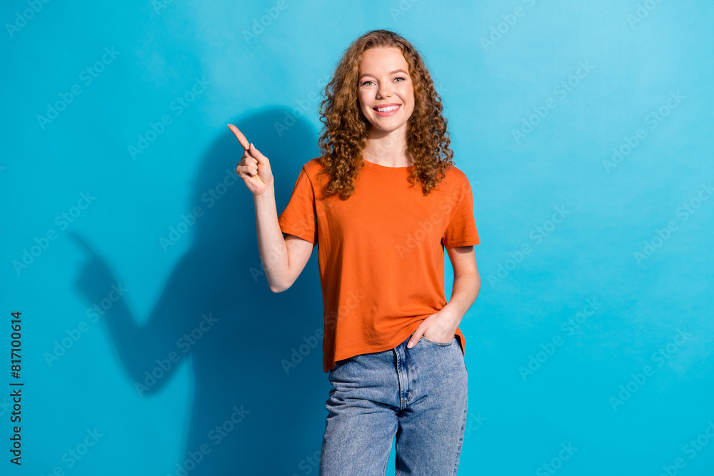 Photo of cheerful red haired youngster student girl in orange t shirt and jeans directing finger new outfits store isolated on blue color background Photo of cheerful red haired youngster student girl in orange t shirt and jeans directing finger new outfits store isolated on blue color background
