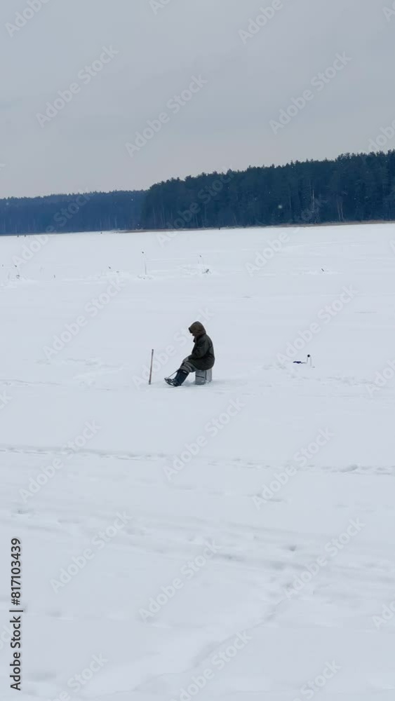 Fishermen on a winter fishing trip catch fish. Winter ice fishing. A winter fisherman is fishing on the pond. A man is sitting on the ice with a camping box, a drill and a thermos. Udmurtia. 4K	