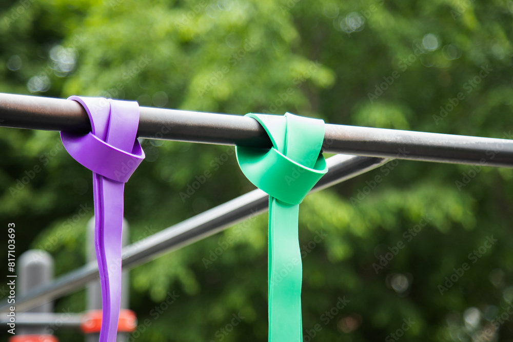 Purple and green Elastic rubber bands for exercise tied on a horizontal bar . Horizontal shot . Close up view
