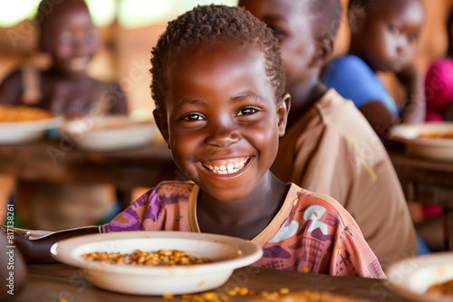 young african boy eating lunch in school smiling at camera with his classmates in background