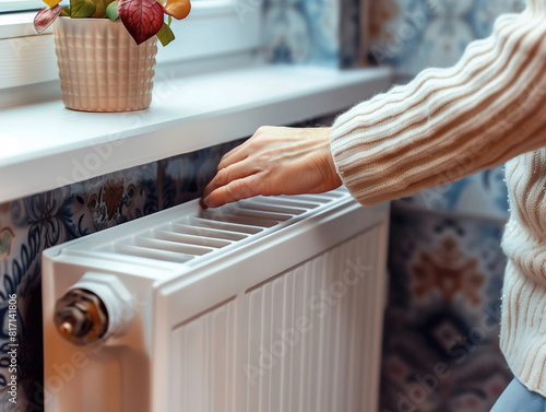 A person warming their hands on a white radiator in a cozy, warmly lit room. Seeking comfort and warmth in a cozy home during cold weather.