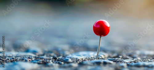 A red pin is stuck in the ground on a grey surface. The pin is the only object in the image, and it is the only thing that stands out. The image has a simple and minimalistic feel