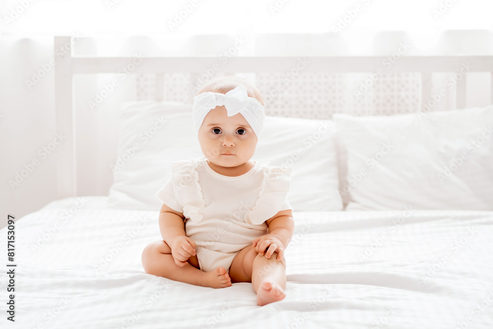Cute newborn baby girl sitting on a bed in white clothes in a br Cute newborn baby girl sitting on a bed in white clothes in a br