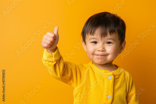 Happy young child in a yellow sweater giving a thumbs up against a vibrant yellow backdrop, showing enthusiasm and positivity