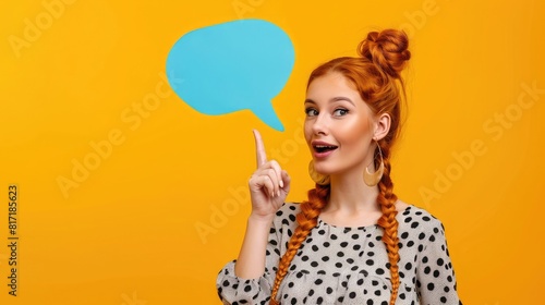 Portrait of beautiful ginger woman with braids holding blue empty comic text bubble above head pointing finger to side wearing cow print top isolated on yellow background,