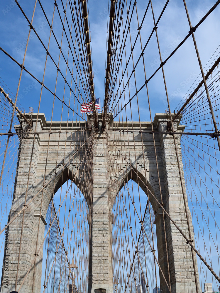 Fototapeta premium Brooklyn bridge with a flag on top of it. The bridge is very old and has a lot of wires