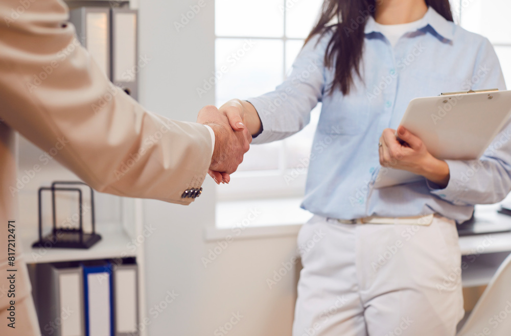 Two company employees man and woman shaking hands standing in office celebrating success, making a good deal, business achievement, signing a contract or greeting new employee on their workplace. Two company employees man and woman shaking hands standing in office celebrating success, making a good deal, business achievement, signing a contract or greeting new employee on their workplace.