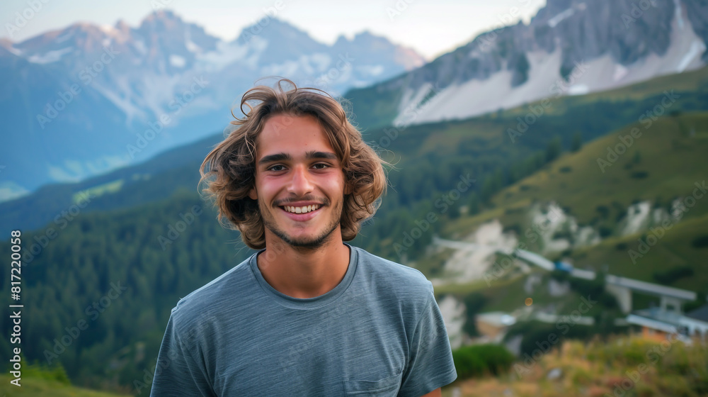 A smiling young man, long-haired in a grey tee, stands against the stunning backdrop A smiling young man, long-haired in a grey tee, stands against the stunning backdrop