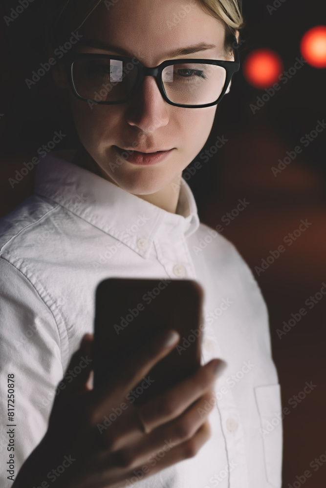 Female standing at Interactive kiosk with smartphone in hand. Young woman reading information on mobile phone while using application at night on city street. Hipster girl with cellphone in darkness