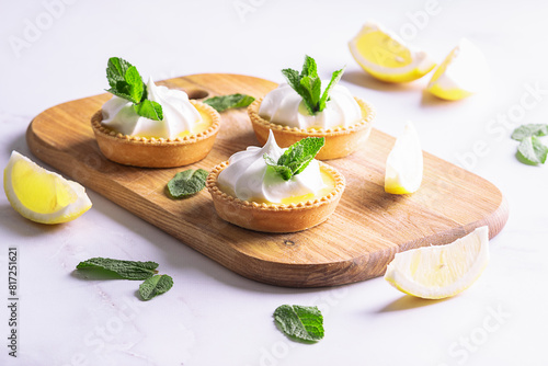 Aromatic homemade lemon tartlets with cream and mint leaves on white marble table close up.