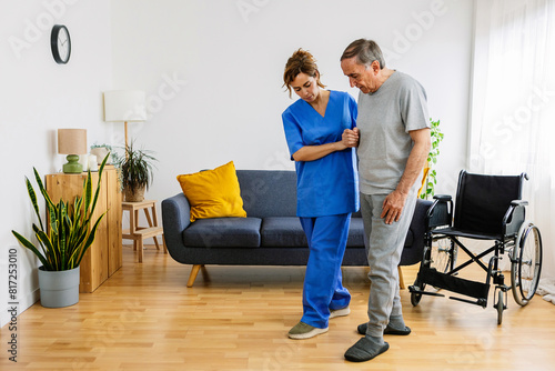 Young adult nursing home helping older man to move at domestic room. Medical female worker in medical uniform supporting senior adult man wheelchair. © Xavier Lorenzo