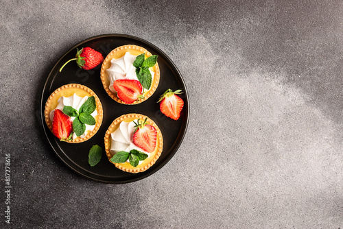 Fresh homemade tart with cream, strawberries and mint leaves on dark stone background with copy space for your design top view.