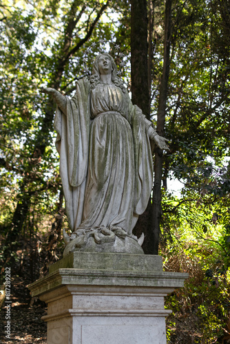 Obraz na płótnie Life-size antique Roman sculpture of a woman in a tunic made of gray stone on a pedestal in a summer green park w salonie