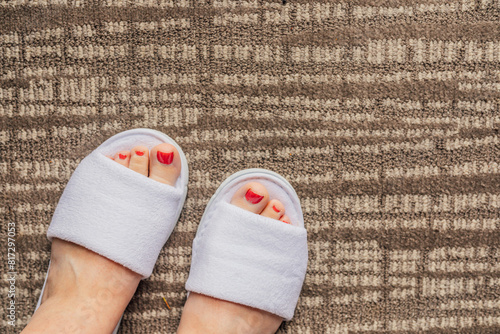 feet with red pedicure in white hotel slippers on carpet
