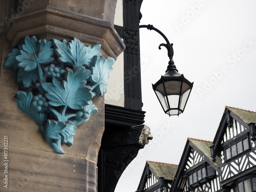 Details of grape leafs on a stone pillar and an old lamp on a building on the rows in Chester with old half timbered buildings in the background