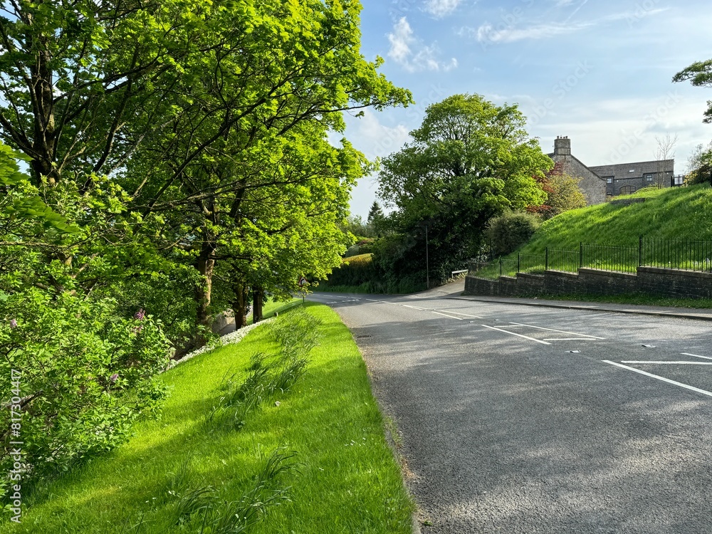 The Colne and Broughton road lined by green trees and grass, leads towards a building in the distance under a clear blue sky in the pretty village of, Thornton-in-Craven, Yorkshire, UK The Colne and Broughton road lined by green trees and grass, leads towards a building in the distance under a clear blue sky in the pretty village of, Thornton-in-Craven, Yorkshire, UK