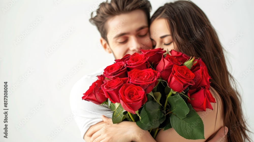 A lovely image captures a romantic couple against a pristine white backdrop The stunning young woman embraces her boyfriend clutching a gorgeous bunch of red roses A lovely image captures a romantic couple against a pristine white backdrop The stunning young woman embraces her boyfriend clutching a gorgeous bunch of red roses