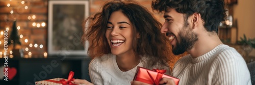 An affectionate couple laughs joyfully while exchanging Christmas gifts photo