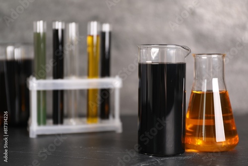 Beakers, flask and test tubes with different types of oil on grey textured table, closeup photo
