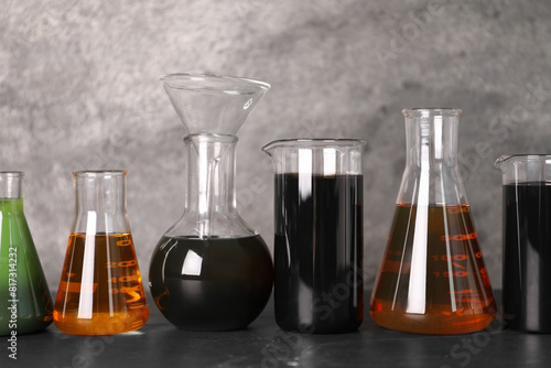 Beakers and flasks with different types of oil on grey textured table photo