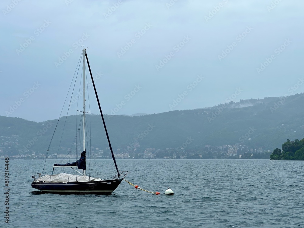 Picturesque View of a Moored Sailboat on Lake Maggiore with Lush Mountainous Landscape in the Background, Verbania, Italy Picturesque View of a Moored Sailboat on Lake Maggiore with Lush Mountainous Landscape in the Background, Verbania, Italy